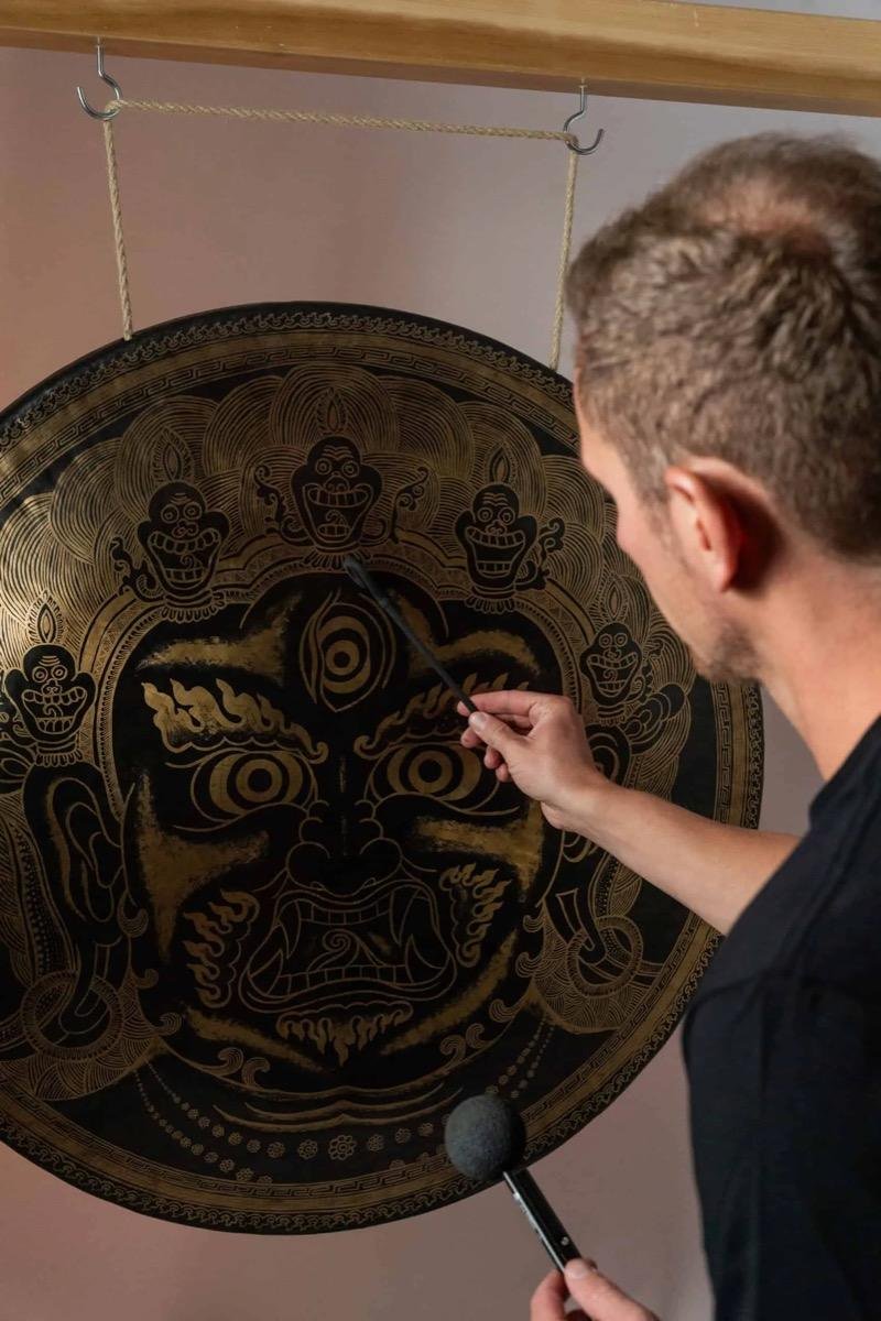 Jens raakt met een mallet een grote gong aan waarop een gouden gravure staat